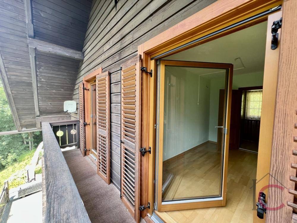 Heller Raum mit Holzboden und Zugang zu einem Balkon mit Blick ins Grüne.