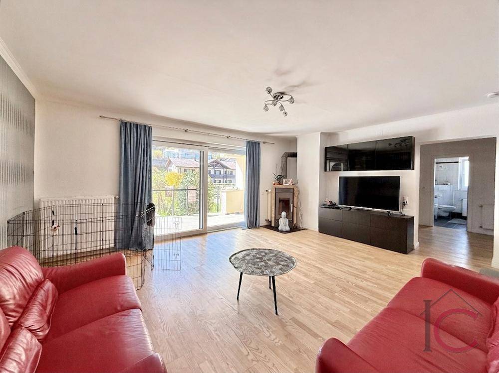 Helles Wohnzimmer mit Holzboden, roten Sofas und direktem Zugang zu einem sonnigen Balkon.