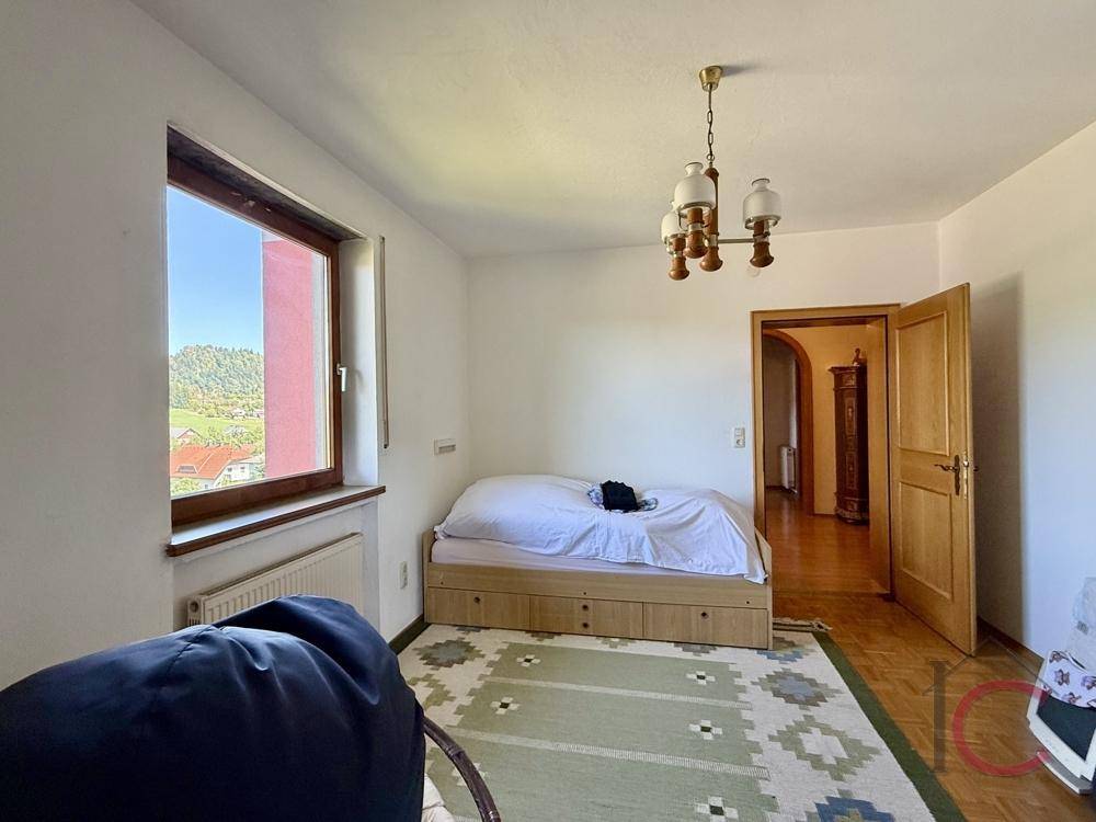 Helles Schlafzimmer mit Einzelbett, Holzparkettboden und großem Fenster mit Ausblick.