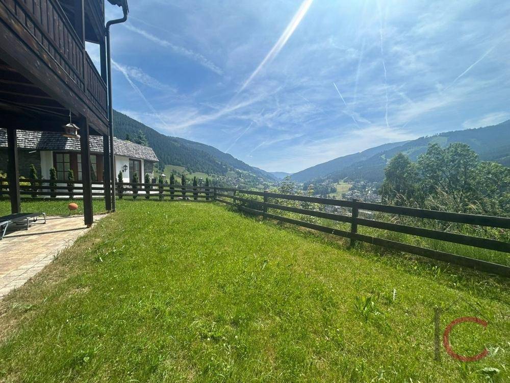 Gepflegte Rasenfläche mit Terrasse und einem weiten Blick über das grüne Tal und die umliegenden Berge.