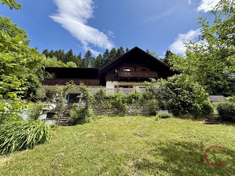 Traditionelles Haus mit Holzfassade und Balkonen, eingebettet in eine grüne Hanglandschaft.