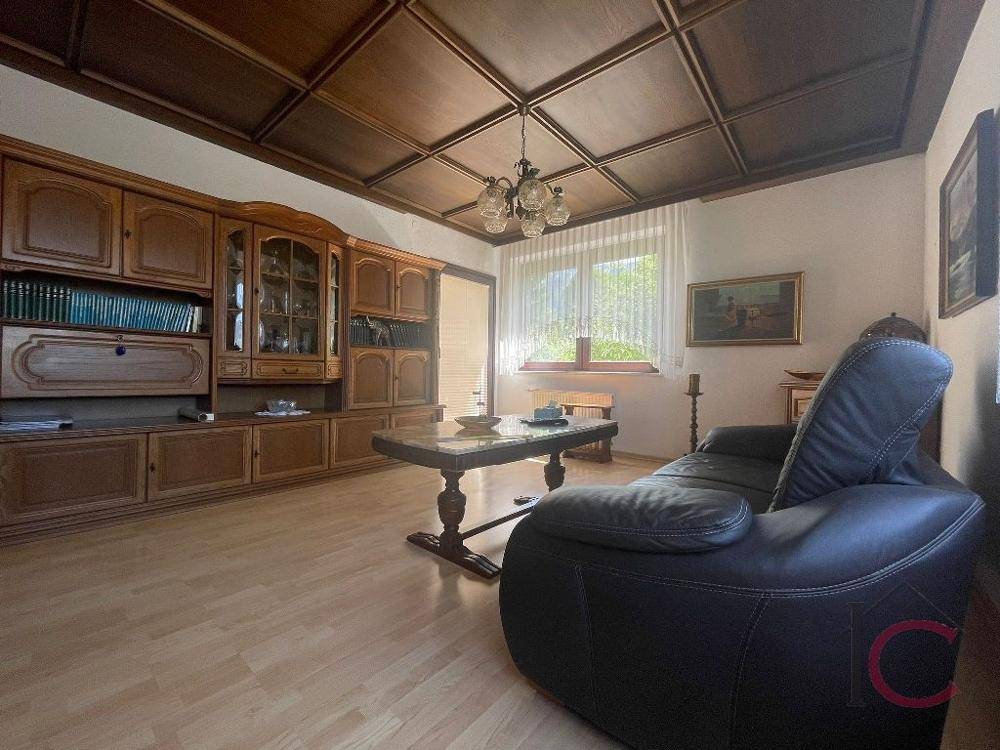 Geräumiges Wohnzimmer mit traditionellen Holzmöbeln, Kassettendecke und Parkettboden.