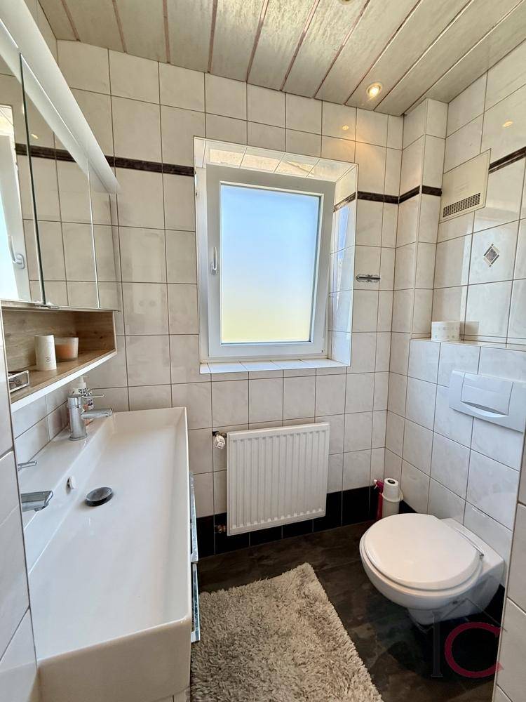 Kleines Gäste-WC mit Waschbecken, Toilette, Spiegelschrank und Fenster für natürliche Belüftung.