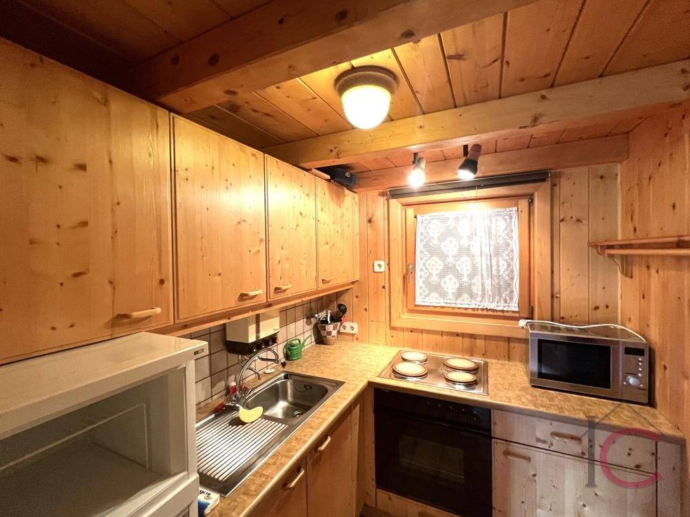 Kleine, funktionale Küche mit Holzschränken, Fenster und grundlegenden Küchengeräten.