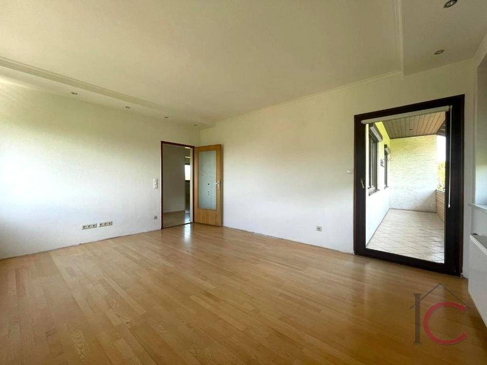 Helles Wohnzimmer mit Holzboden und Zugang zu einem überdachten Balkon oder Loggia.