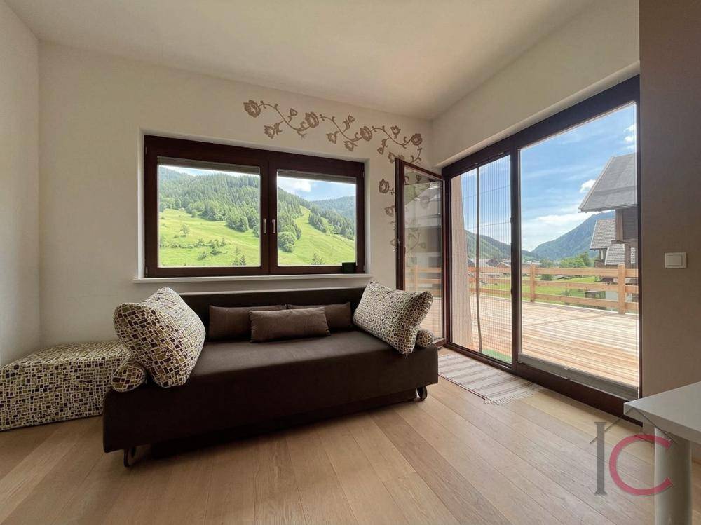 Gemütliches Wohnzimmer mit Sofa, Holzboden und direktem Zugang zur sonnigen Terrasse mit Bergblick.