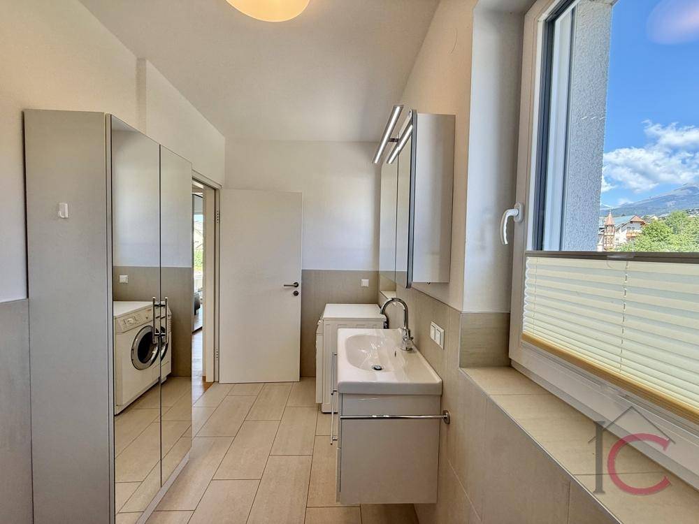 Geräumiges Badezimmer mit Waschmaschine, Waschbecken, Spiegelschrank und großem Fenster.