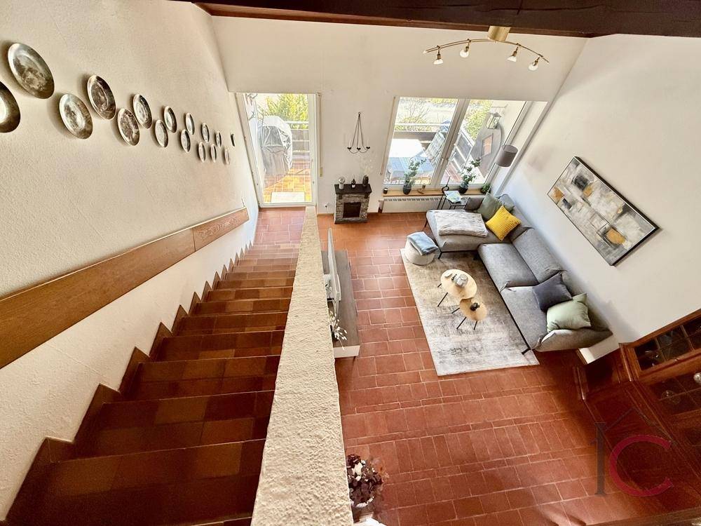 Treppenhaus mit Fliesenstufen, das zum offenen Wohnbereich mit hohen Decken führt.