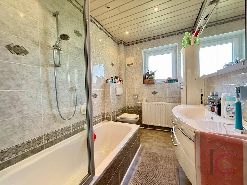 Funktionales Badezimmer mit Badewanne, integrierter Dusche, Waschbecken und Fenster für Tageslicht.