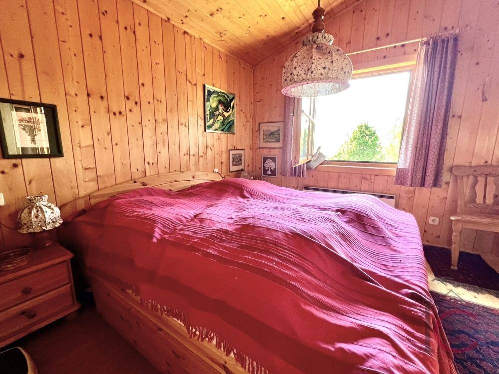 Schlafzimmer mit Holzwänden, großem Bett und Fenster mit Blick ins Grüne.