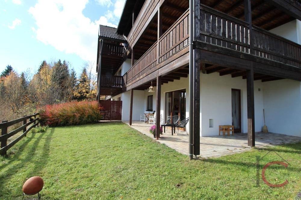 Gebäudeseite mit mehreren Holzbalkonen und einer gepflasterten Terrasse im Erdgeschoss.