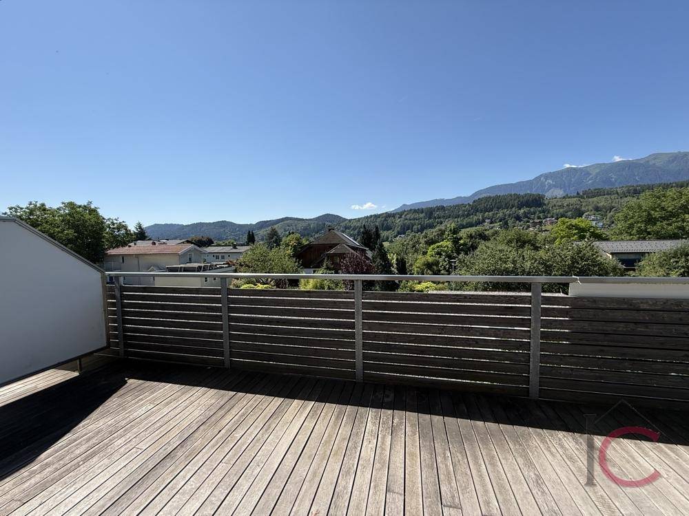 Weitläufige Holzterrasse mit Panoramablick auf die grüne Hügellandschaft und die Berge.