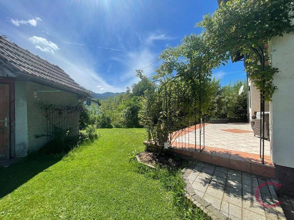 Übergang von der Terrasse zum grünen Gartenbereich mit einem kleinen Gartenhaus im Hintergrund.