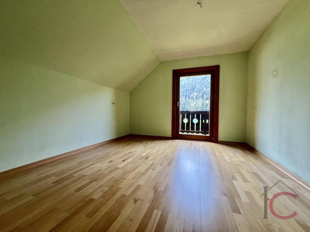 Schlafzimmer mit Holzboden, Dachschräge und Zugang zu einem kleinen Balkon.