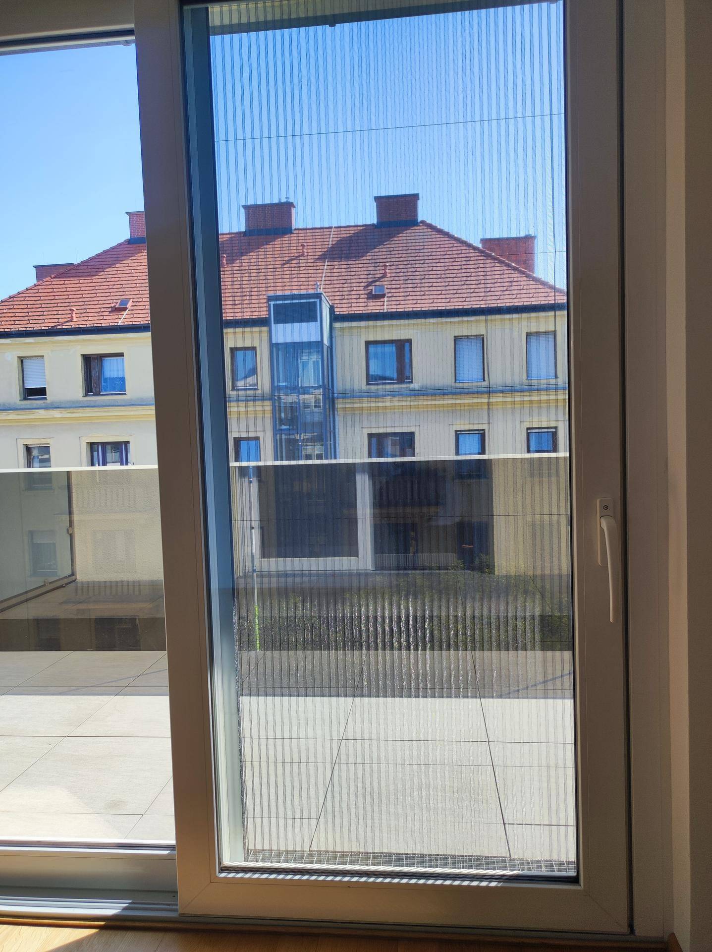 Blick vom Wohnzimmer auf die Terrasse und das gegenüberliegende Gebäude mit Aufzug.