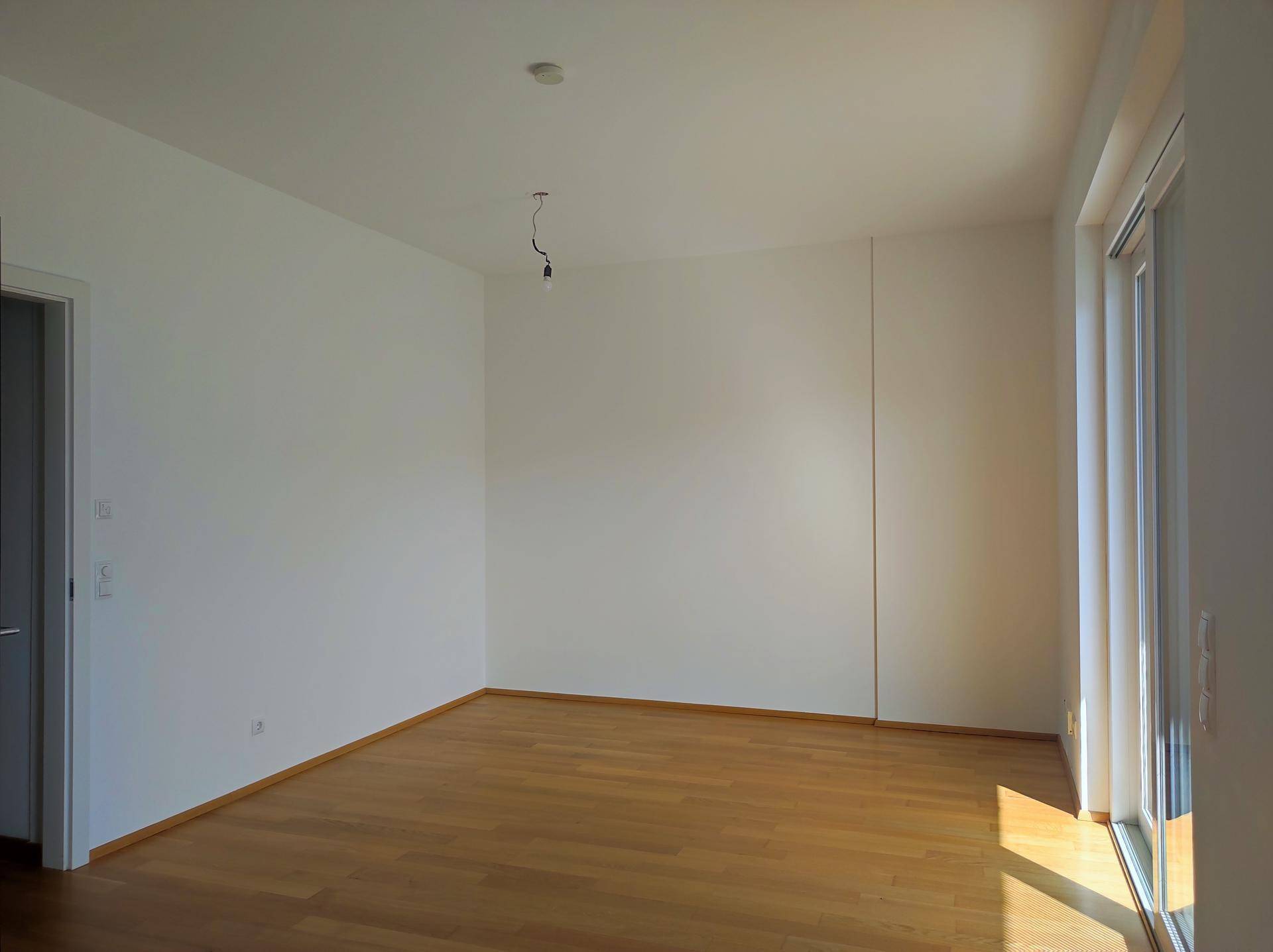 Geräumiges, helles Wohnzimmer mit Holzboden und großen Fenstern, bereit zur Einrichtung.