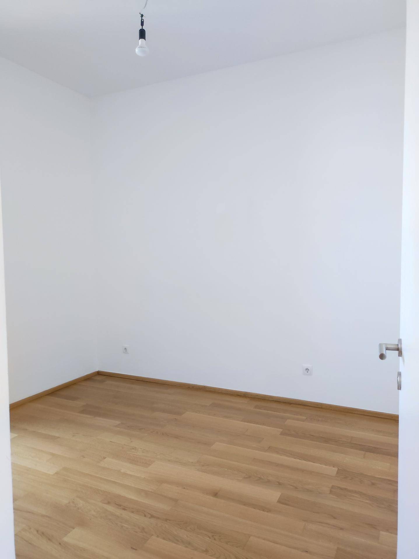 Leeres Schlafzimmer mit Holzboden und weiß gestrichenen Wänden, bereit zur individuellen Gestaltung.