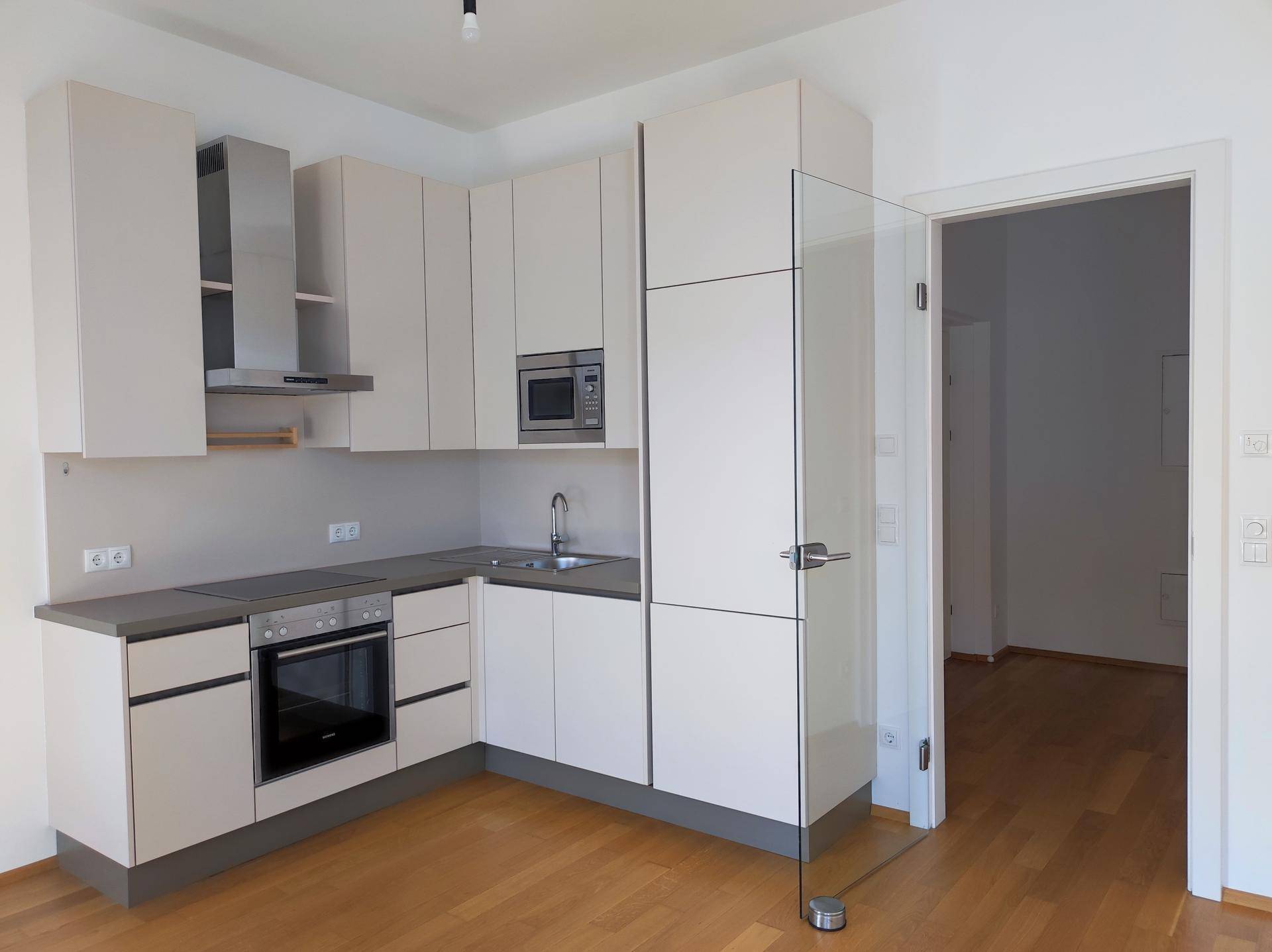 Moderne Einbauküche in hellem Beige mit integrierten Geräten und Holzboden.