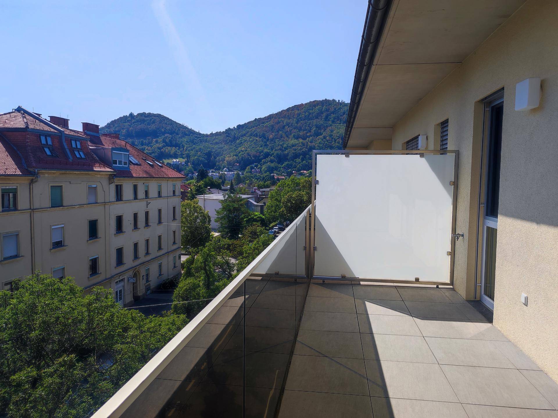 Sonniger Terrassenbereich mit weitem Blick über die Stadt und die umliegenden grünen Hügel.