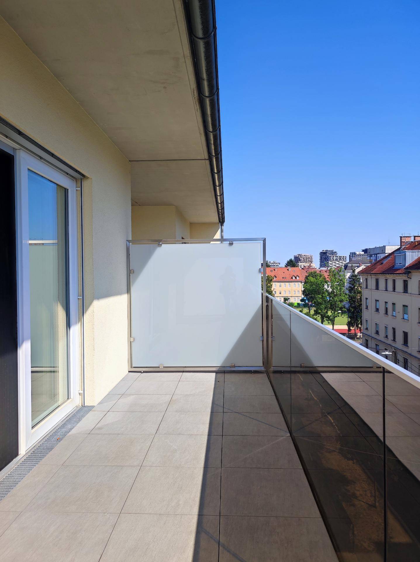 Helle Dachterrasse mit modernen Fliesen und Glasgeländer, bietet viel Platz im Freien.