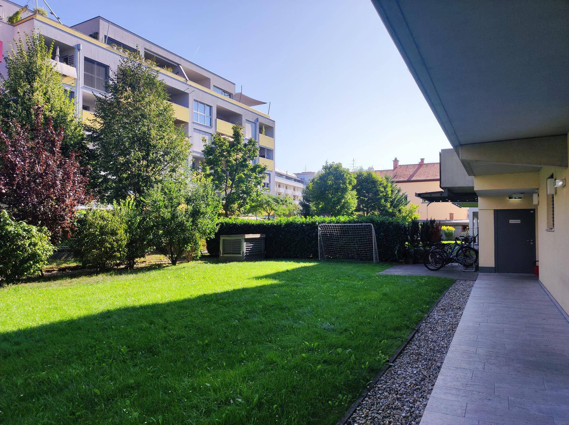 Gepflegter Gemeinschaftsgarten mit Rasenfläche, Bäumen und einem kleinen Fußballtor.
