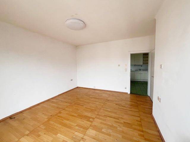 Geräumiger Wohnbereich mit hellem Parkettboden und Zugang zur Küche.