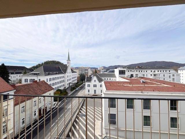 Weitläufiger Stadtblick von einem Balkon mit Blick auf Gebäude, Straßen und entfernte Berge.