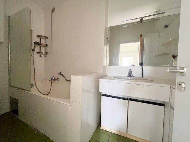 Badezimmer mit Badewanne, Duschabtrennung, Waschbecken und grünem Fliesenboden.