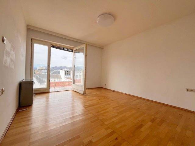 Heller Wohnraum mit Parkettboden und großen Fenstertüren zum Balkon.