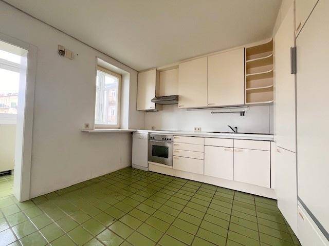 Helle Küche mit beigen Einbauschränken, grünem Fliesenboden und Fenster.