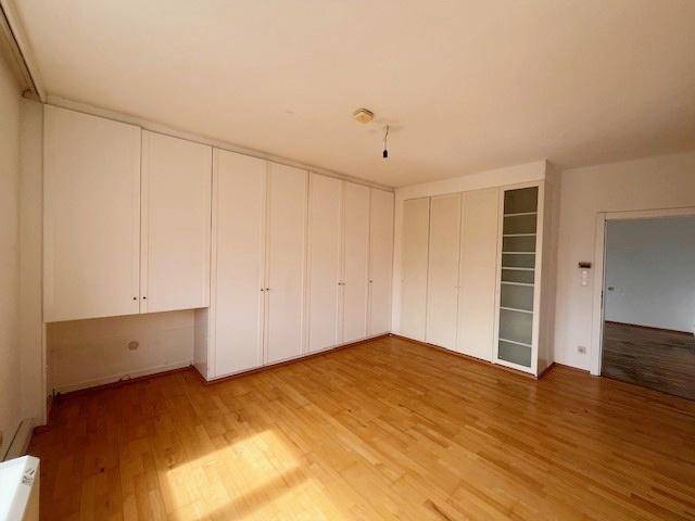 Schlafzimmer mit umfangreichen weißen Einbauschränken und hellem Parkettboden.
