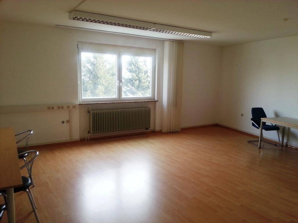 Heller, leerer Büroraum mit großem Fenster, Laminatboden und Heizkörper, bereit zur individuellen Gestaltung.