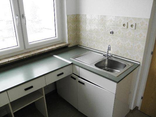 Kleine Küchenzeile mit Spüle, Unterschränken und gefliestem Spritzschutz unter einem Fenster.