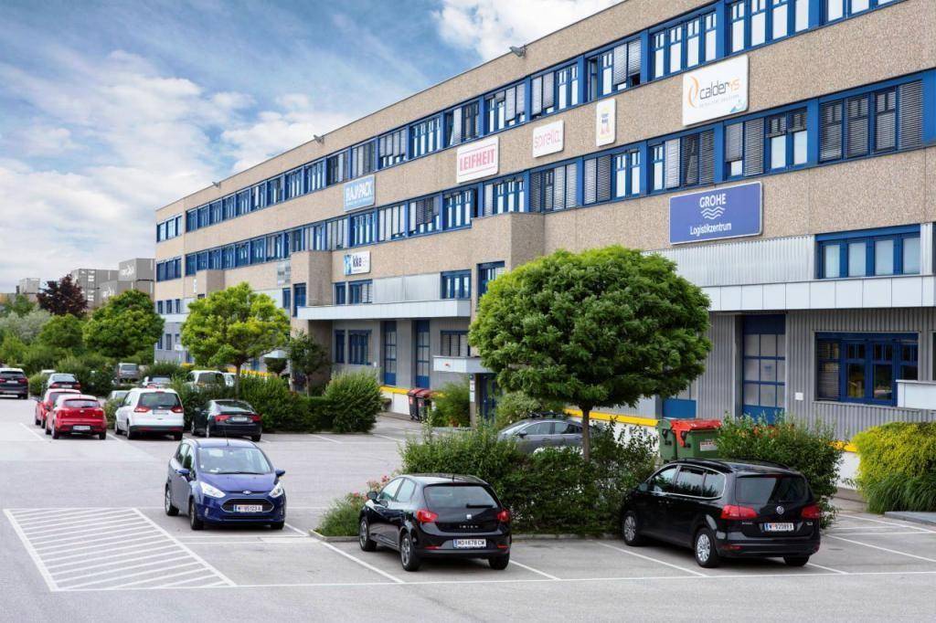 Mehrstöckiges Geschäftsgebäude mit vielen Fenstern und einem Parkplatz davor unter bewölktem Himmel.
