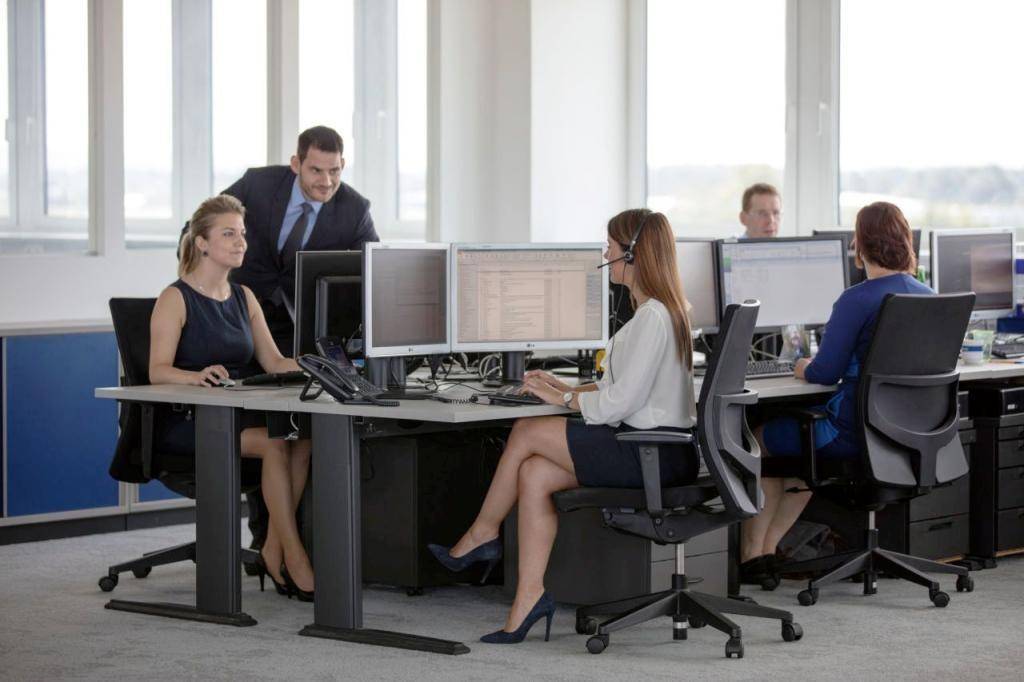 Offenes Büro mit mehreren Arbeitsplätzen, Computern und Mitarbeitern, die an ihren Schreibtischen arbeiten.
