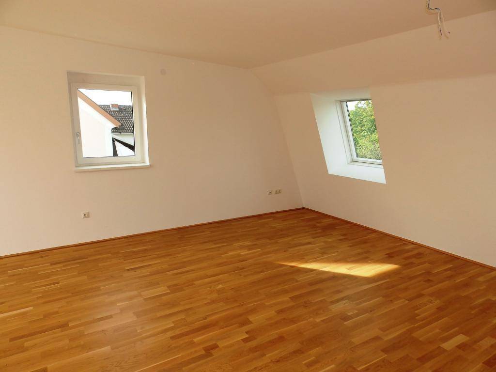 Geräumiges Zimmer mit Parkettboden und zwei Fenstern, eines davon ein Dachfenster.