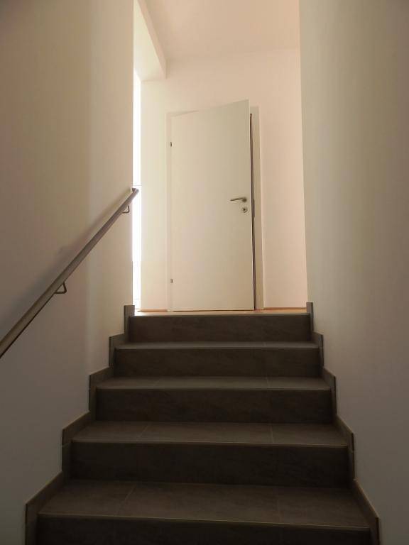 Treppenaufgang mit Fliesenstufen und schlichtem Geländer, führt in die obere Etage.