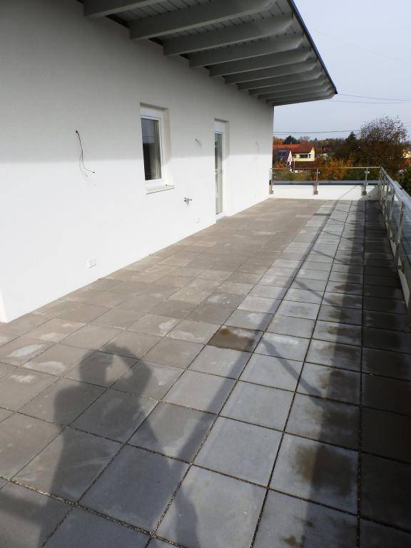 Weitläufige Außenterrasse mit Fliesenboden und moderner Glasbrüstung, ideal zum Entspannen.