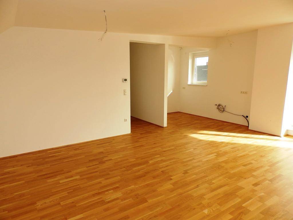 Offener Wohnbereich mit Parkettboden und Zugang zu einem weiteren Raum, lichtdurchflutet.