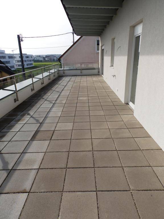 Breite Terrasse mit Fliesenboden und moderner Glasbrüstung, bietet viel Platz im Freien.