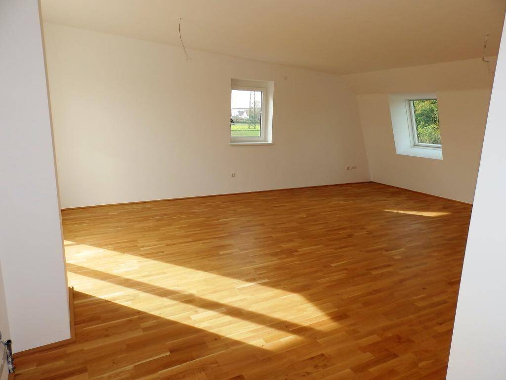Geräumiges Zimmer mit Parkettboden und zwei Fenstern, eines davon ein Dachfenster.