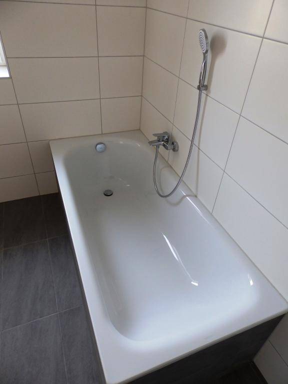Nahaufnahme der Badewanne mit integrierter Duscharmatur und modernen Fliesen.