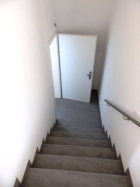 Blick von oben auf den Treppenabgang mit Fliesenstufen und Handlauf.