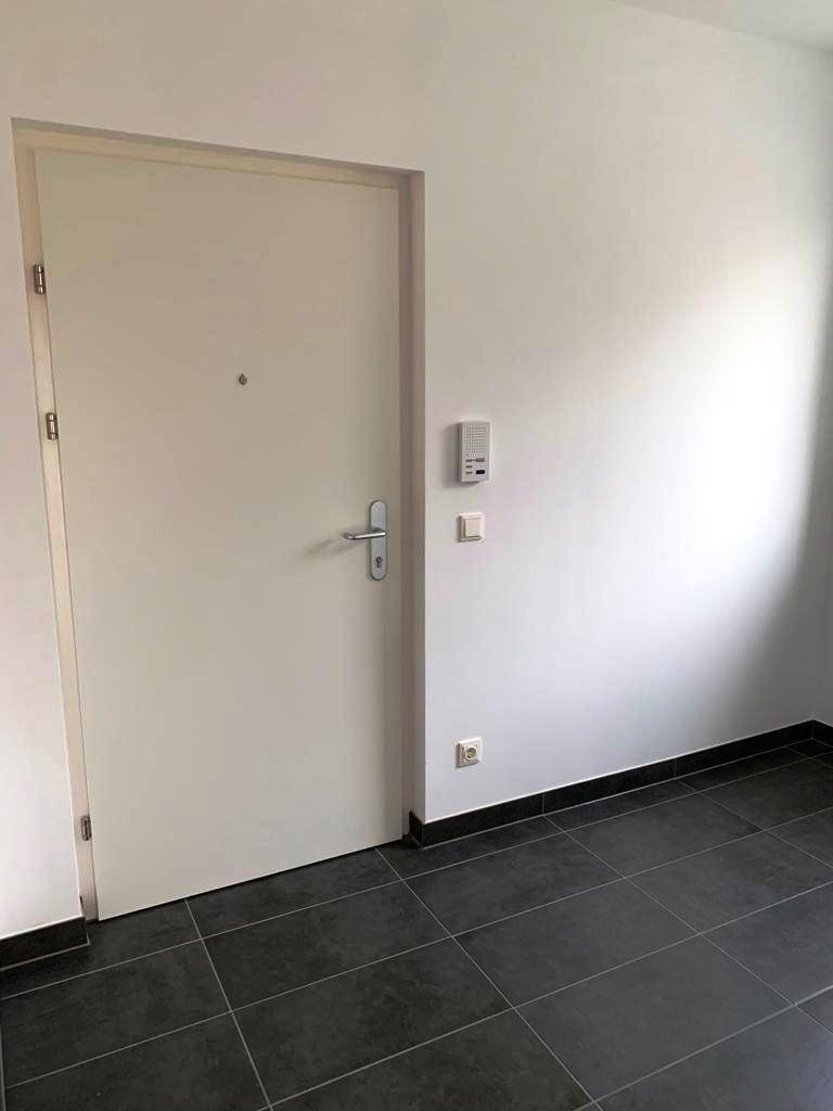 Eingangsbereich mit dunklen Fliesen, einer weißen Tür und einer Gegensprechanlage an der Wand.