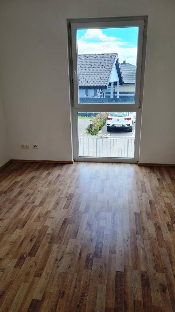 Helles Schlafzimmer mit Laminatboden und einem Fenster mit Blick auf den Parkplatz.