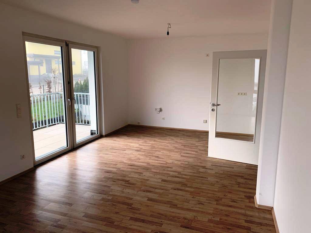 Heller Wohnraum mit Laminatboden und großen Fenstern, die Zugang zu einem Balkon bieten.