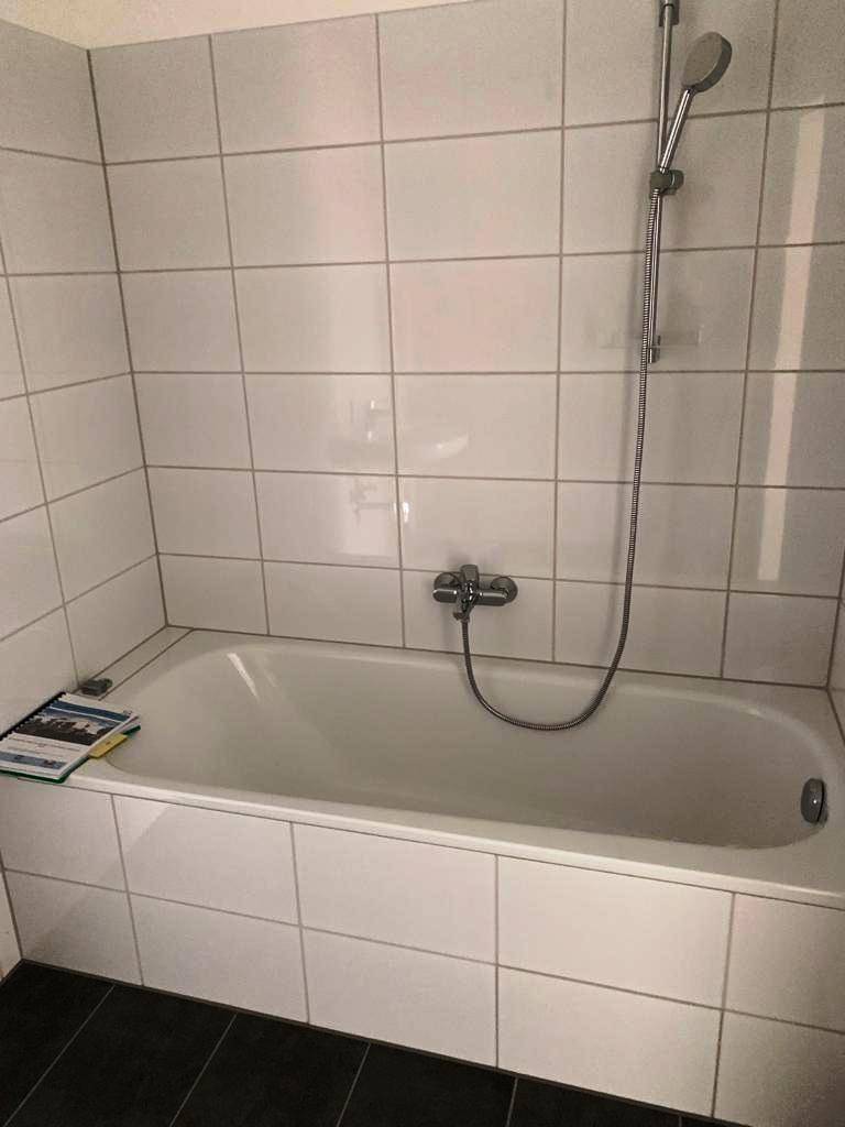 Badezimmer mit einer Badewanne und weißen Wandfliesen, ausgestattet mit einer Duscharmatur.