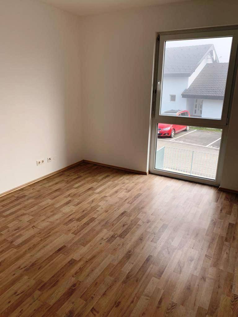 Helles Schlafzimmer mit Laminatboden und einem Fenster, das einen Blick nach draußen ermöglicht.