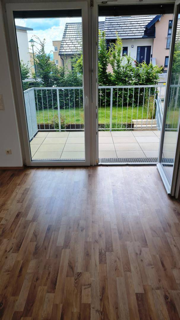 Heller Wohnraum mit Laminatboden und Zugang zu einem Balkon mit Grünblick.