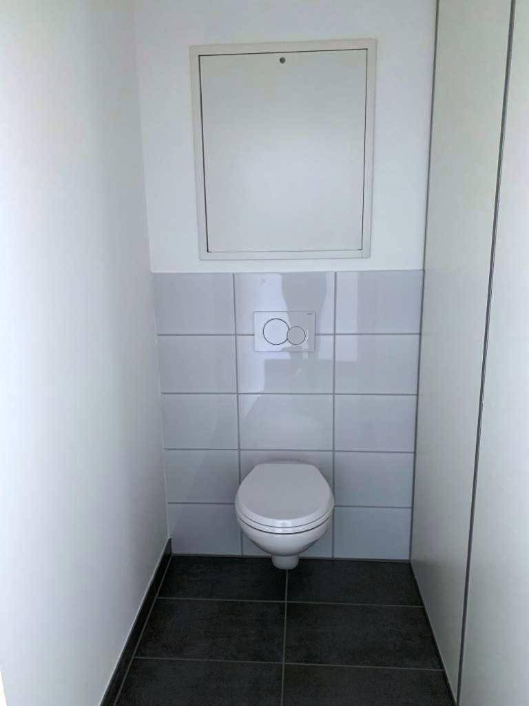 Modernes Gäste-WC mit Wand-WC und weißen Fliesen, in einem sauberen und funktionalen Zustand.